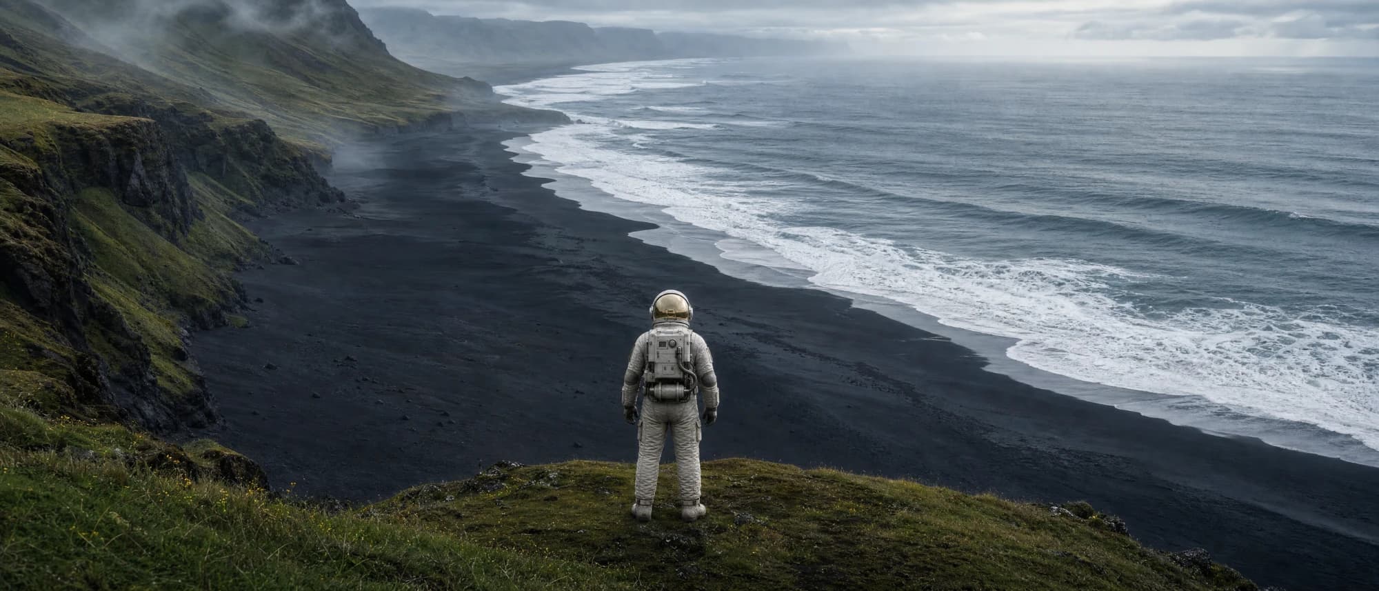 Von einer grünen Klippe blickt der Astronaut auf einen schwarzen Strand und das Meer.